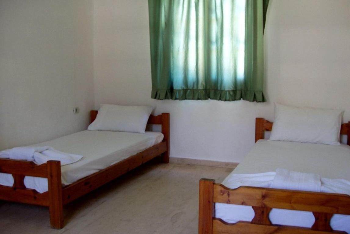 A room with two wooden beds, white bedding, and a window with green curtains.