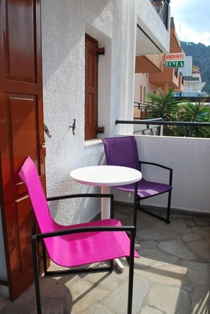 A balcony with two chairs and a small table, a wooden door, and a building with a sign that reads "APARTMENTS." - Koula Apartments (Hersonissos)