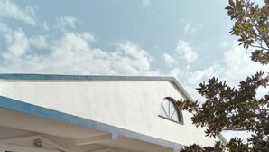 Un edificio de dos pisos con balcón, ventanas amplias y un árbol al frente.