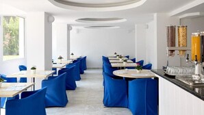 Un restaurante con sillas tapizadas en azul, mesas blancas y un diseño moderno del techo.