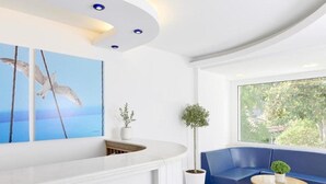 Un área de recepción moderna con un mostrador blanco, un sofá azul y un amplio ventanal con vistas a zonas verdes.