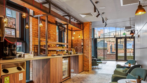 A modern cafe with a wooden counter, a coffee machine, and a recycling bin. - Roomzzz Newcastle (Newcastle-upon-Tyne)