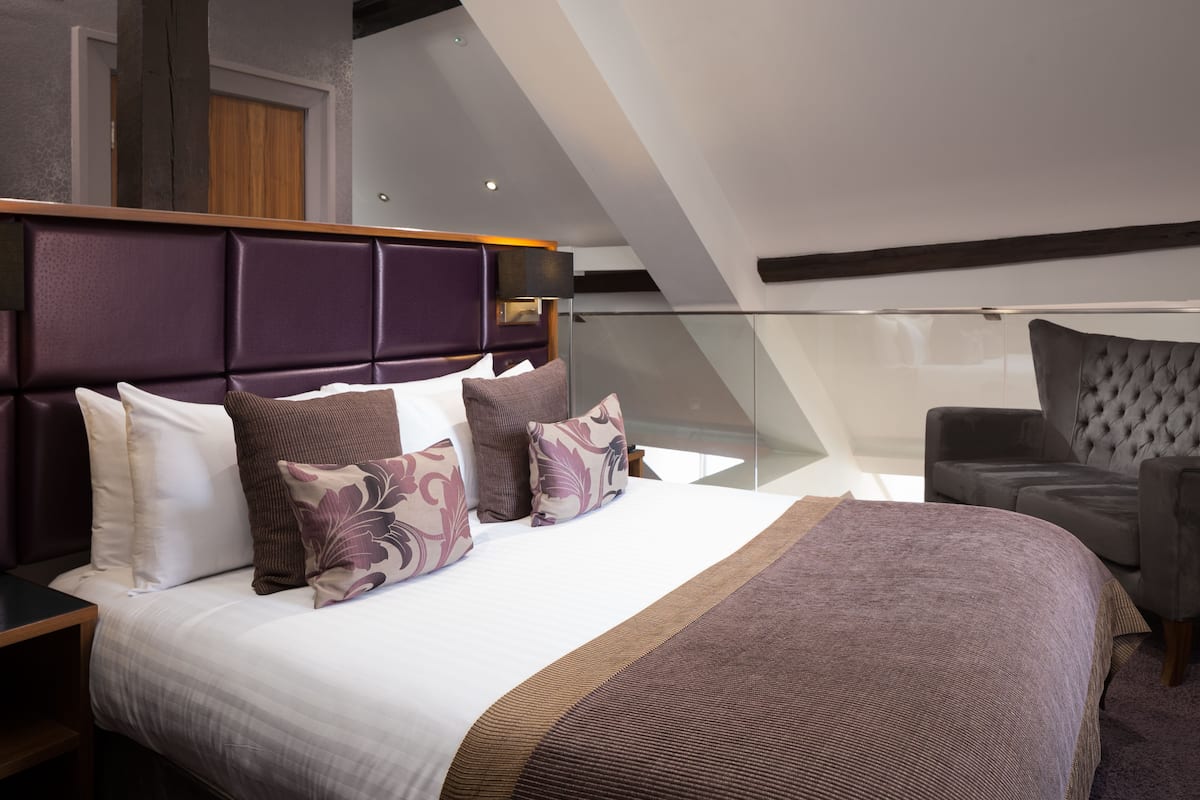 A modern bedroom with a large bed, a glass balcony, and a view of the sky.