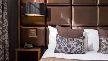 Una habitación de hotel con un cabecero capitonado, una lámpara de noche, un teléfono y almohadas estampadas.