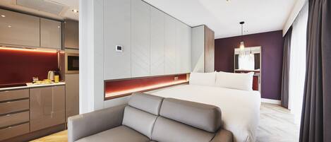 Una habitación de hotel moderna con sofá, cama, kitchenette y un espejo grande.