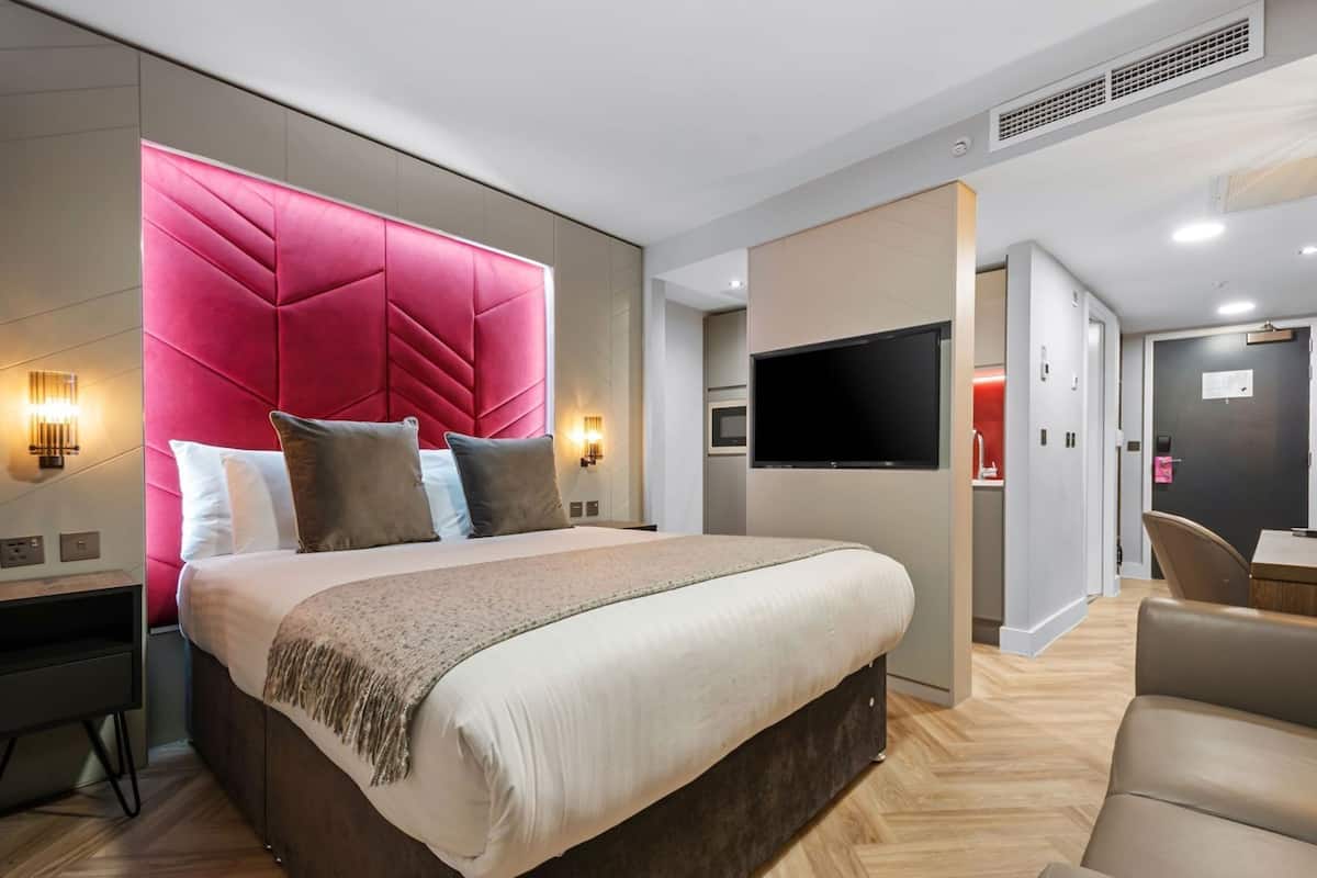 A modern hotel room with a large bed, a flat-screen TV, a desk with a chair, and a separate bathroom.
