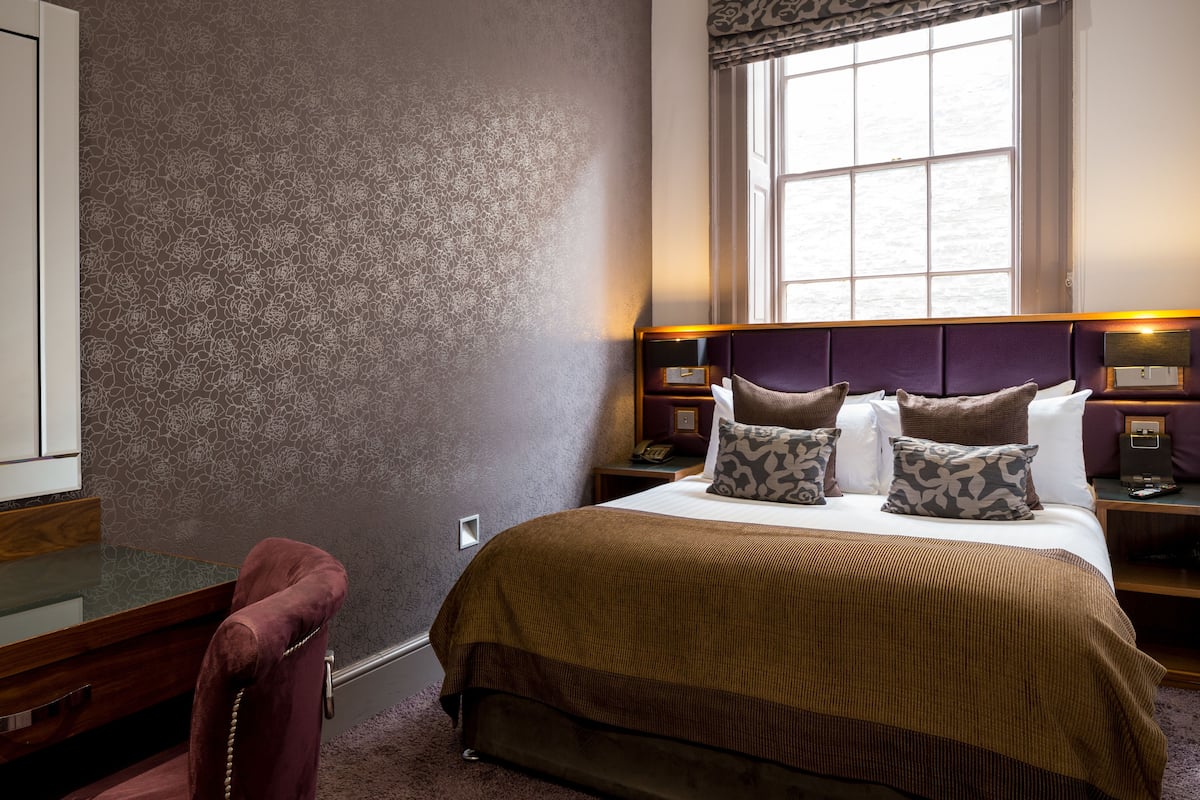 A hotel room with a large bed, a desk, and a chair.
