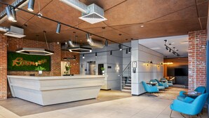 A modern reception area with a white counter, blue seating, and exposed brick walls. - Roomzzz Newcastle (Newcastle-upon-Tyne)