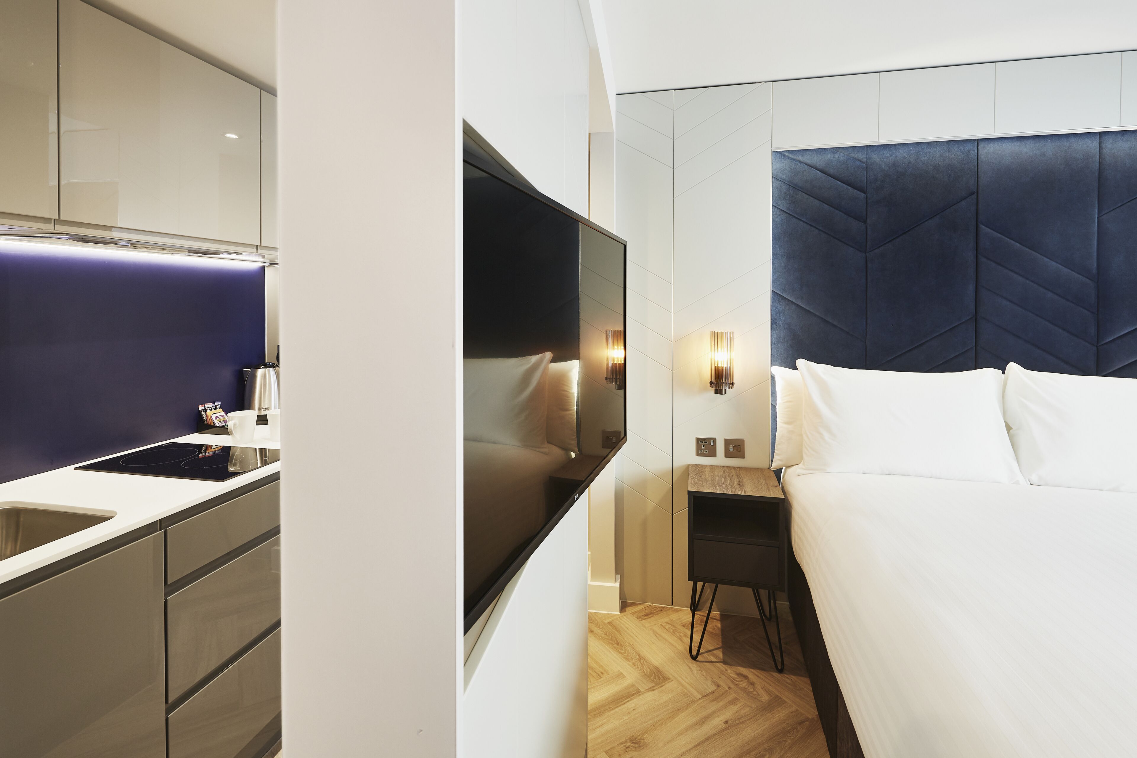 A modern hotel room with a large bed, a flat-screen TV, a bedside table, and a built-in wardrobe.