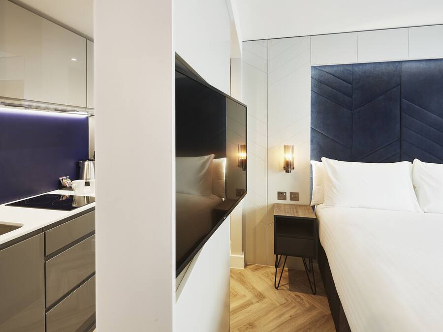 A modern hotel room with a large bed, a flat-screen TV, a bedside table, and a built-in wardrobe.