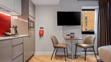 Una habitación de hotel moderna con kitchenette, un televisor de pantalla plana, dos sillas y una cama.