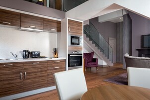 A modern kitchen with wooden cabinets, a microwave, and a built-in oven. There is a staircase leading to an upper level.