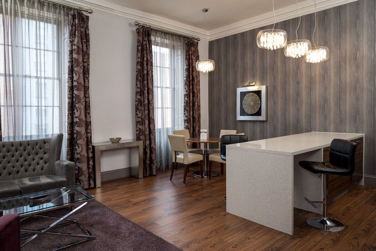 A modern hotel room with a dining area, a bar, and a large window with curtains.