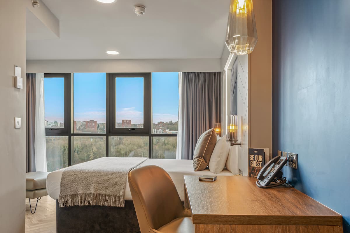 A hotel room with a bed, a desk, a phone, and a view of the city.