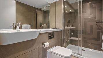 Une salle de bain moderne avec un grand miroir, un lavabo, des toilettes et une douche séparée par des parois en verre.