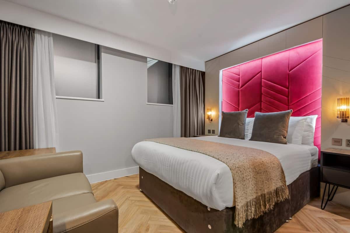 A modern hotel room with a large bed, a desk, and a seating area.