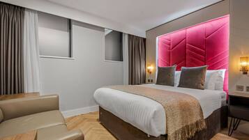 A modern hotel room with a large bed, a desk, and a seating area.
