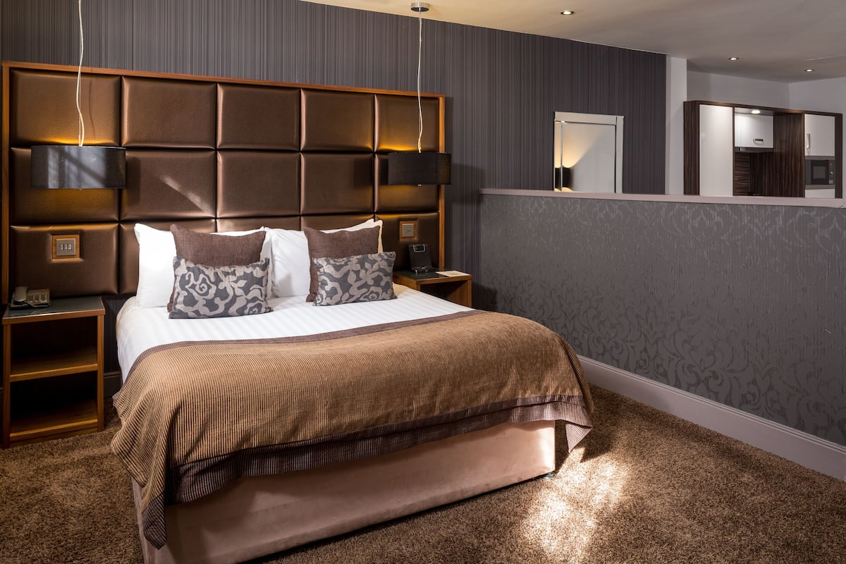 A hotel room with a large bed, a headboard with built-in lighting, a bedside table, and a mirror.