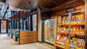 A modern interior with seating areas, a refrigerated display, and a variety of products on shelves. - Roomzzz Newcastle (Newcastle-upon-Tyne)