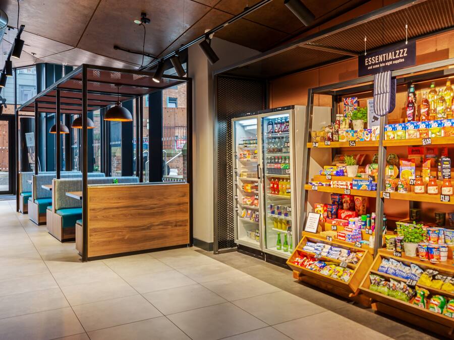 Un interior moderno con zonas de estar, un expositor refrigerado y una variedad de productos en estanterías.