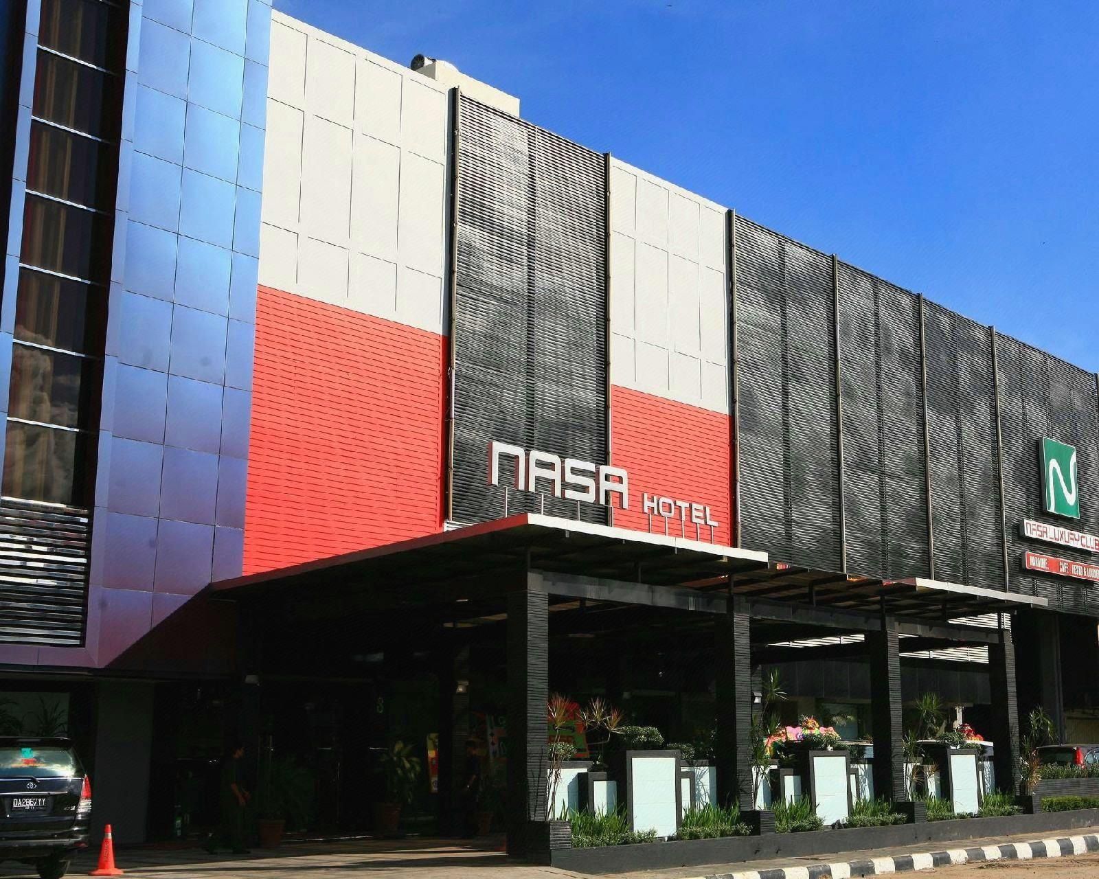 Un edificio moderno con un llamativo letrero 'Nasa Hotel', que presenta una combinación de colores rojo, blanco y negro, y una zona de entrada cubierta con plantas en macetas.