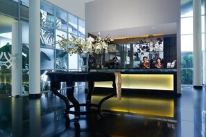 Uma área de recepção com mesa preta, flores brancas e divisória de vidro.