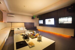 A modern hotel room with a sofa, a coffee table with snacks, a TV, and a minibar.