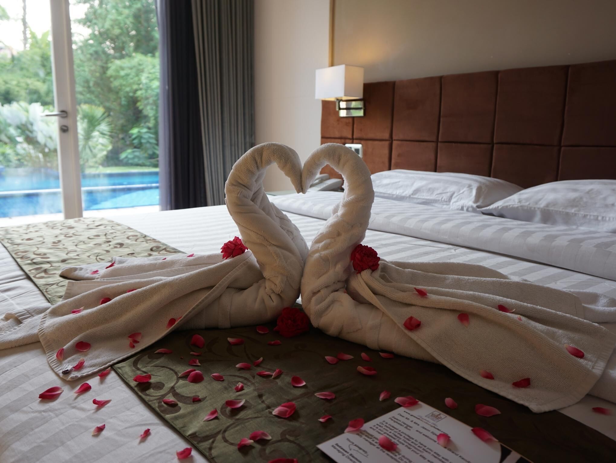 Une chambre d’hôtel avec un lit, une décoration en forme de cœur réalisée avec des serviettes et une vue sur la piscine.