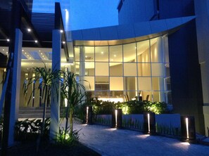A modern building with a glass facade, outdoor seating area, and well-lit entrance.