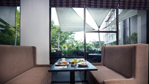 Un espace repas comprenant deux banquettes confortables, une table dressée avec des assiettes de nourriture et des boissons, et une vue sur la verdure grâce à de grandes fenêtres.