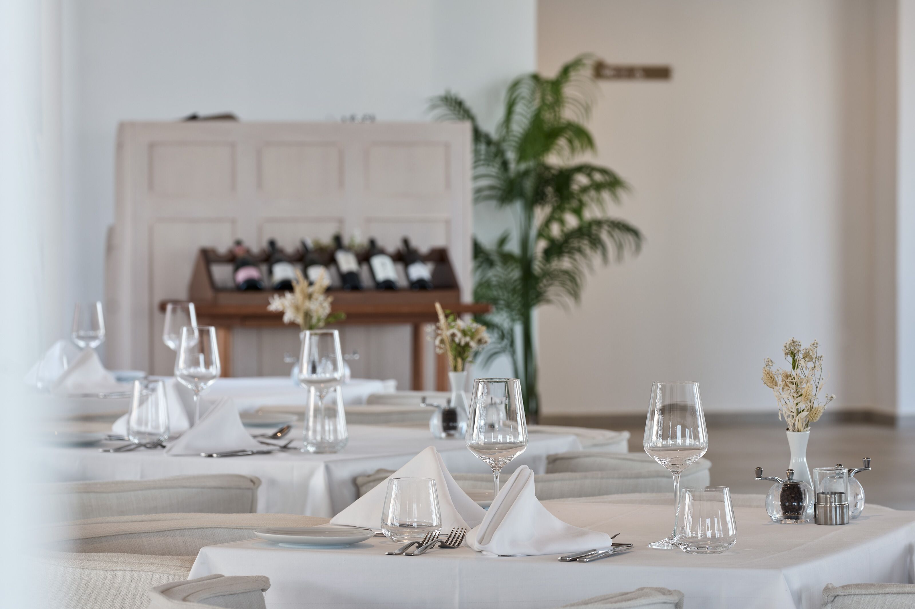 A dining table set with white tablecloths, wine glasses, and a vase with flowers.