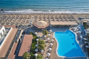 Vista aérea de un complejo turístico con piscina, sombrillas de playa, sillas de descanso y un área de estar cubierta.