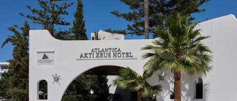 The entrance to the Atlanticia Akti Zeus Hotel with a clear archway and a palm tree in the foreground.