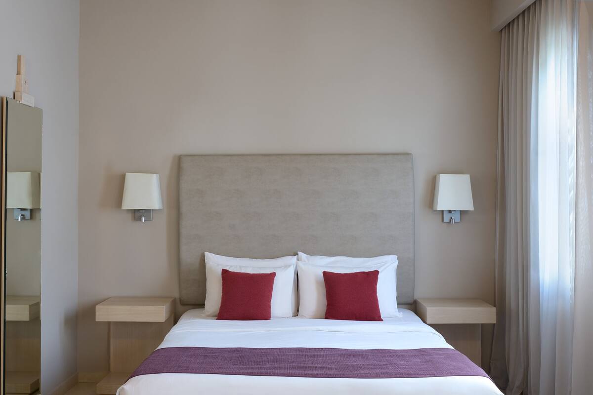 A hotel room with a bed, two nightstands, a headboard, and a window with curtains.