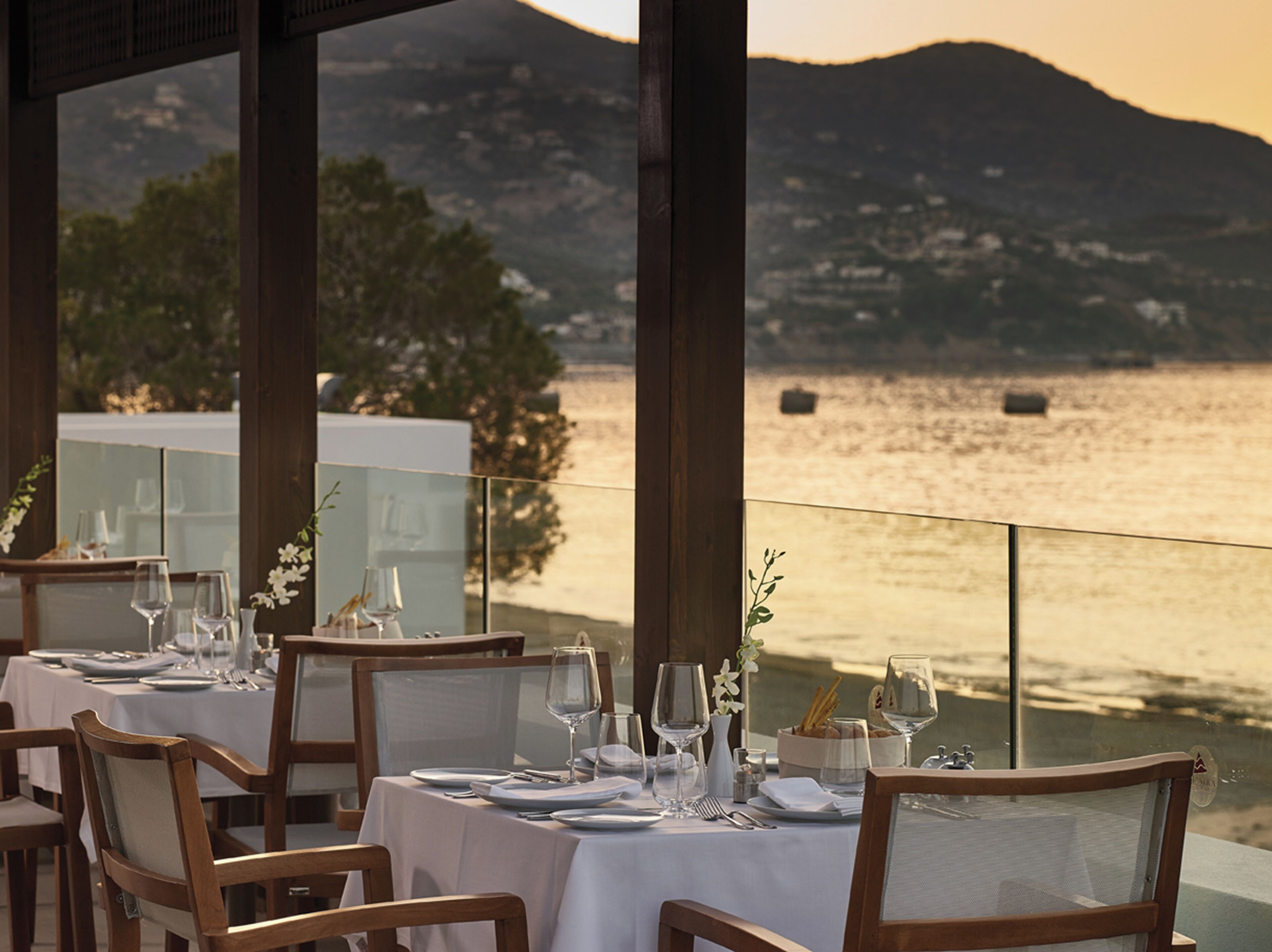 A restaurant with tables set for dining, overlooking a body of water and mountains.