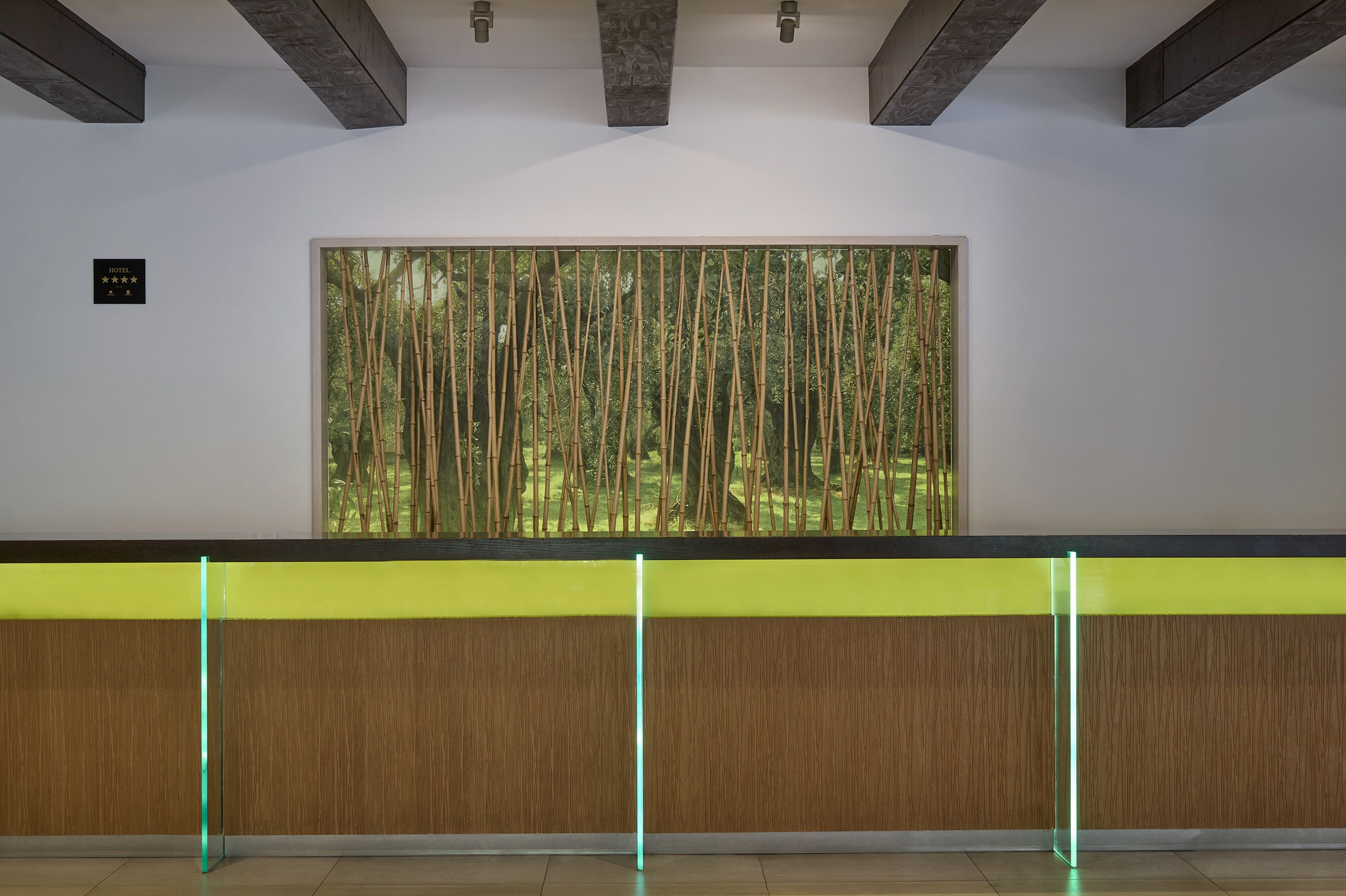 Un área de recepción con un amplio ventanal que muestra bambú, un mostrador de madera y una luz de neón.