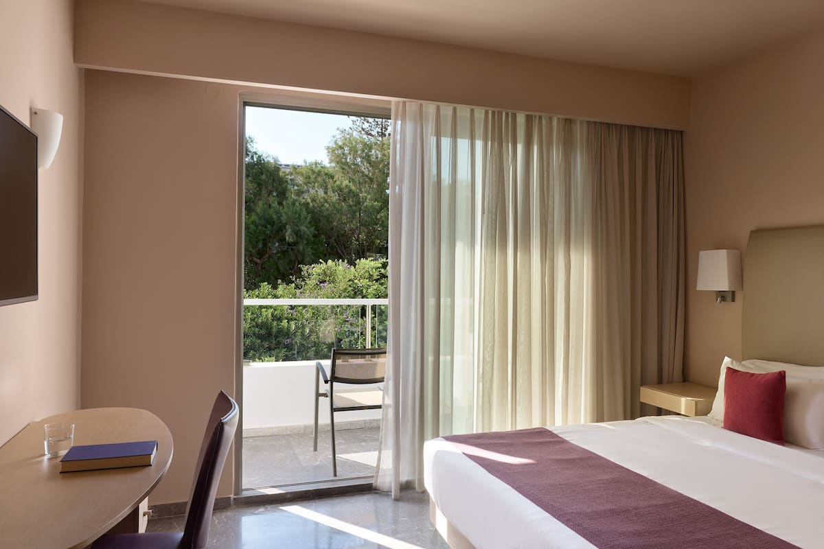 A hotel room with a bed, a desk, a chair, and a view of the outdoors.