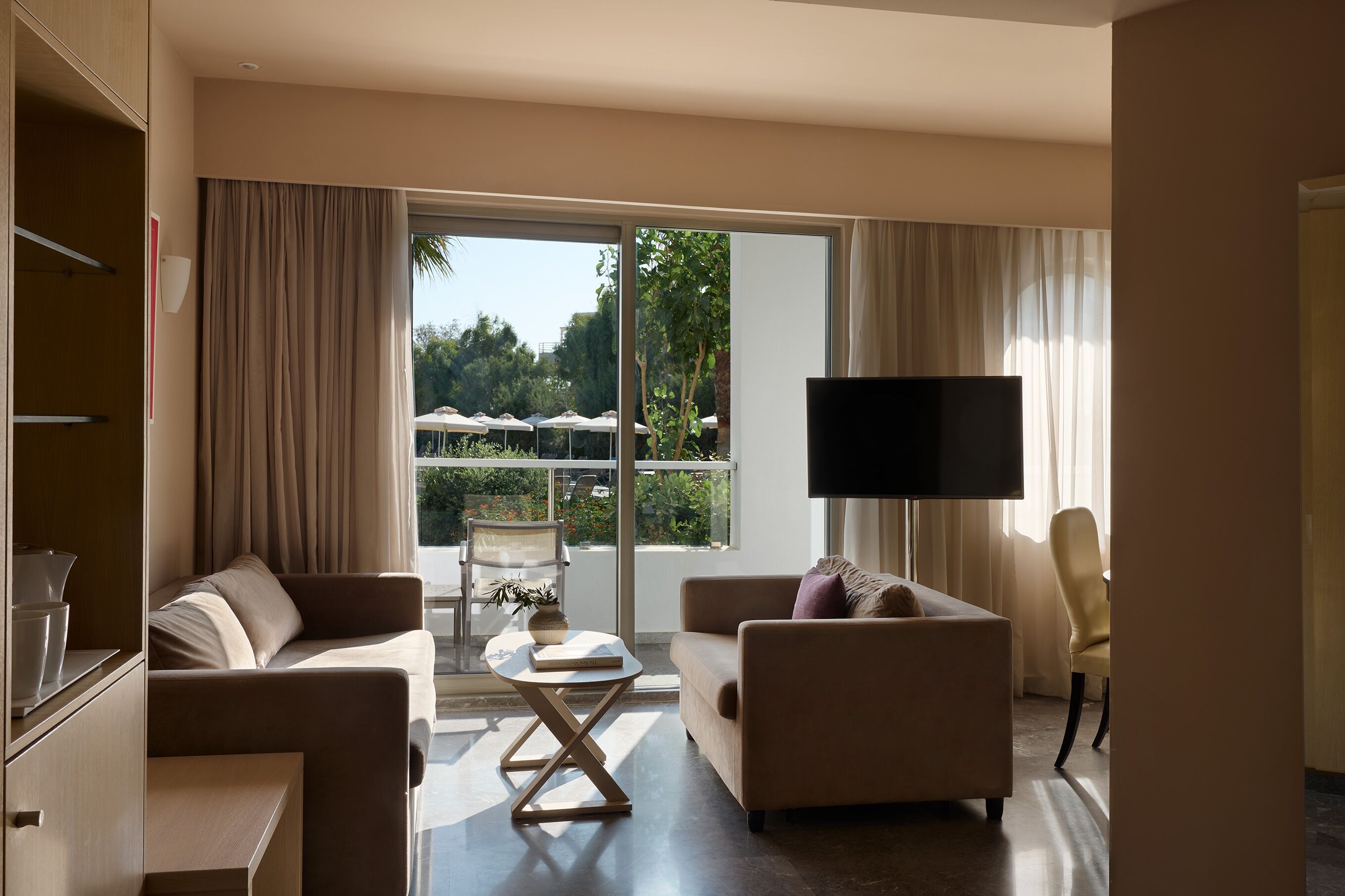 A modern hotel room with a sofa, armchair, and a flat-screen TV.