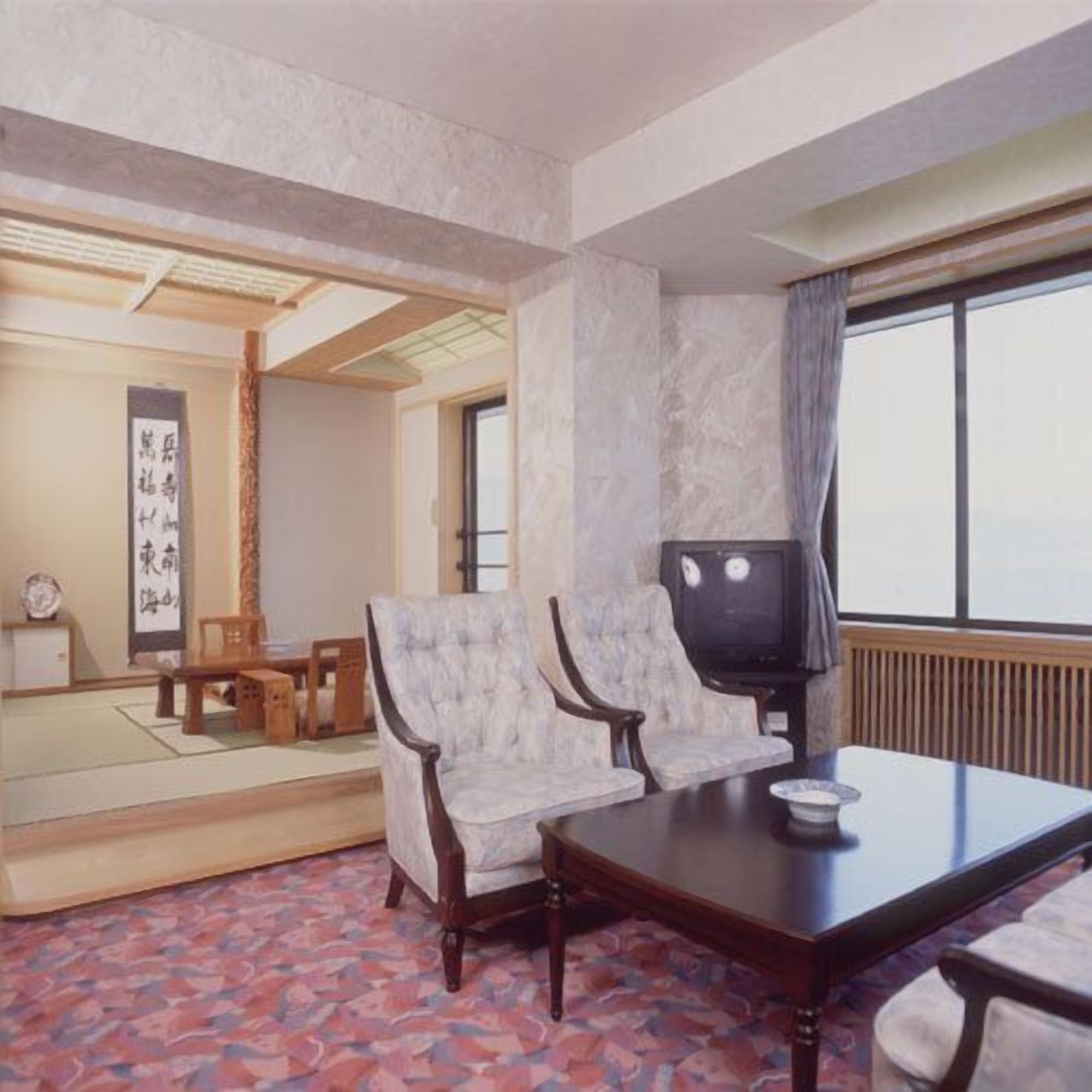 A traditional Japanese room with tatami flooring, a low table, two chairs, a television, and a shoji screen.