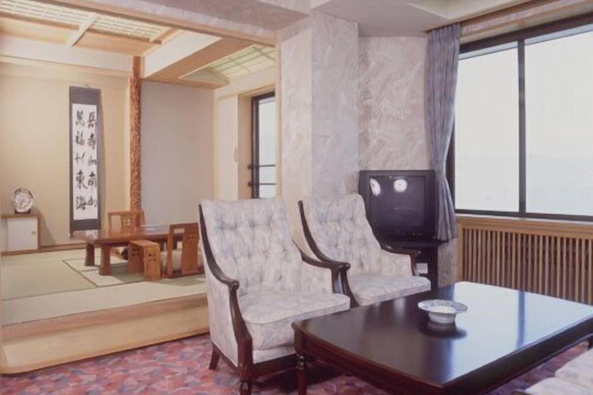 Una habitación japonesa tradicional con suelo de tatami, una mesa baja, dos sillas, un televisor y un biombó shoji.