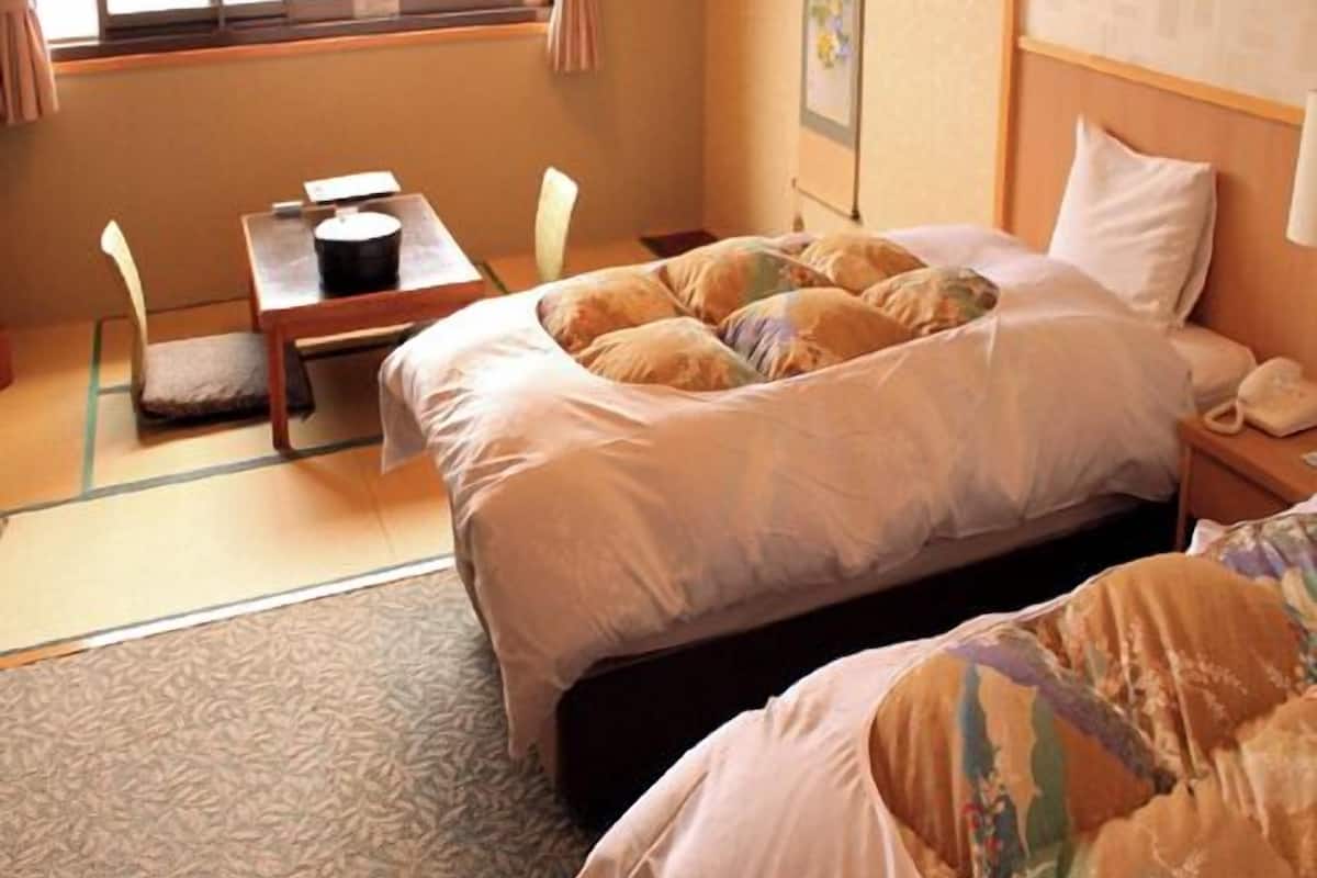 Habitación de hotel con cama, mesita de noche, silla y ventana con cortinas.