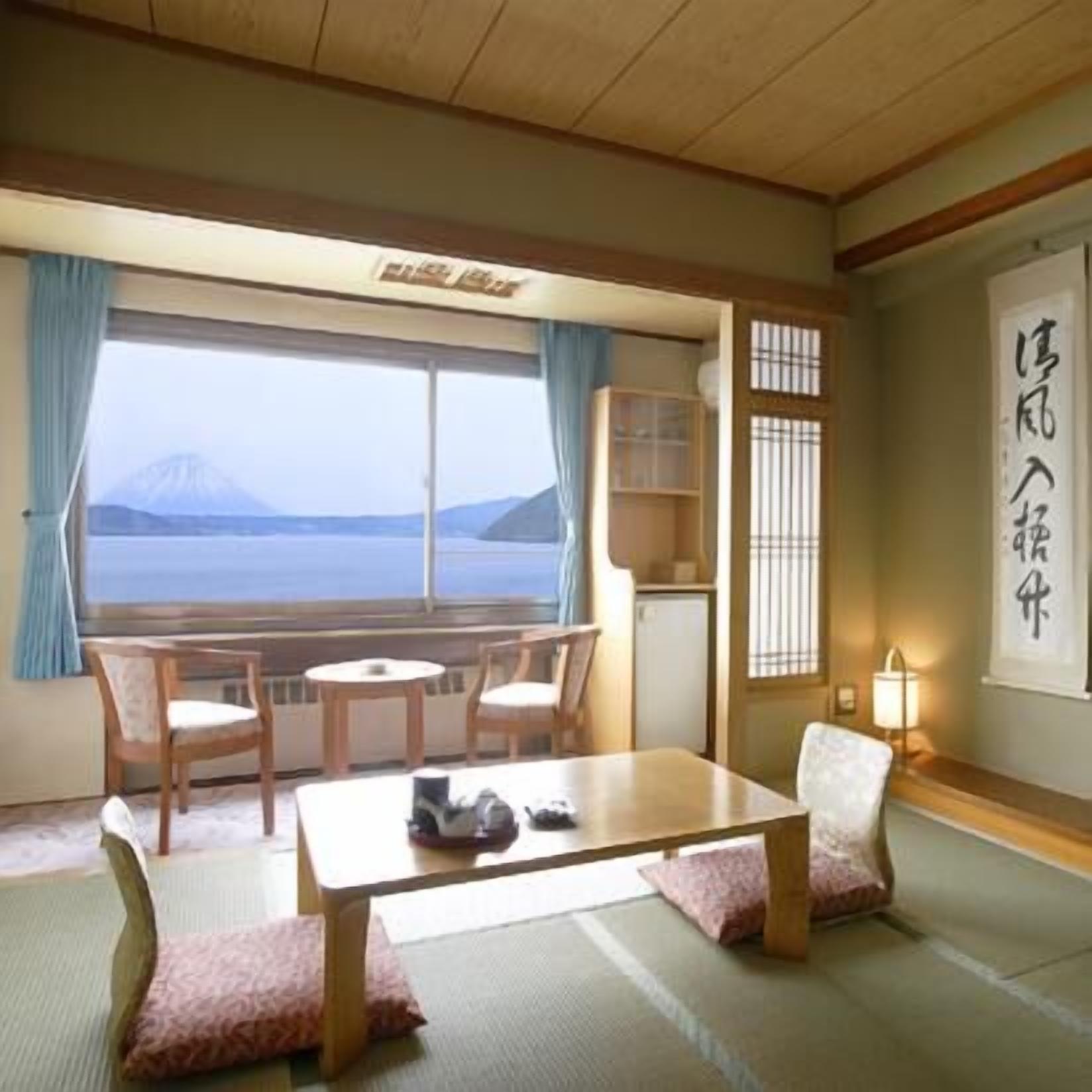 Una habitación con suelo de tatami, una mesa baja, sillas, vista a la montaña y un tradicional puertas correderas japonesas.
