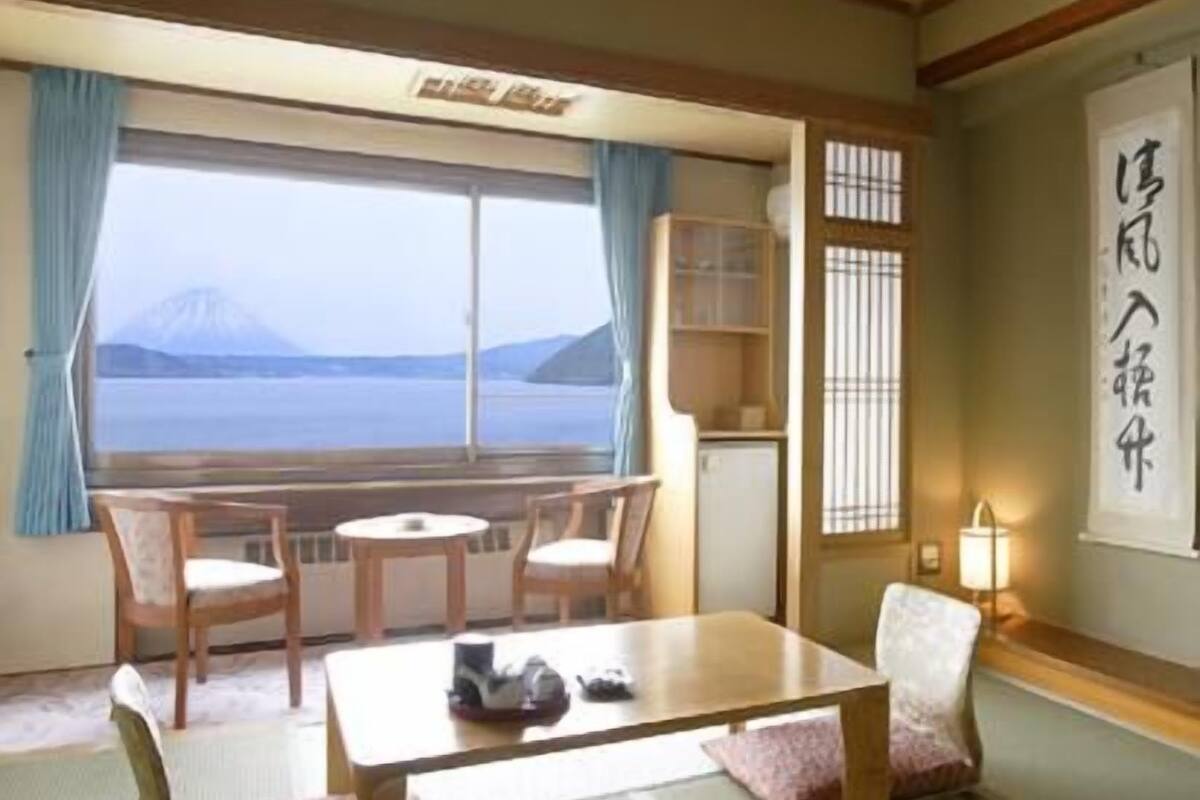 Una habitación con suelo de tatami, una mesa baja, sillas, vista a la montaña y un tradicional puertas correderas japonesas.