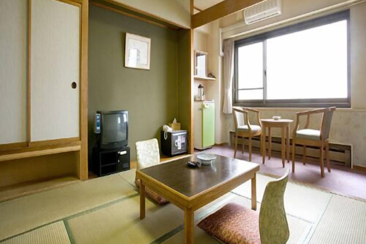 Una habitación japonesa tradicional con suelo de tatami, una mesa baja, un televisor y una ventana con cortinas.
