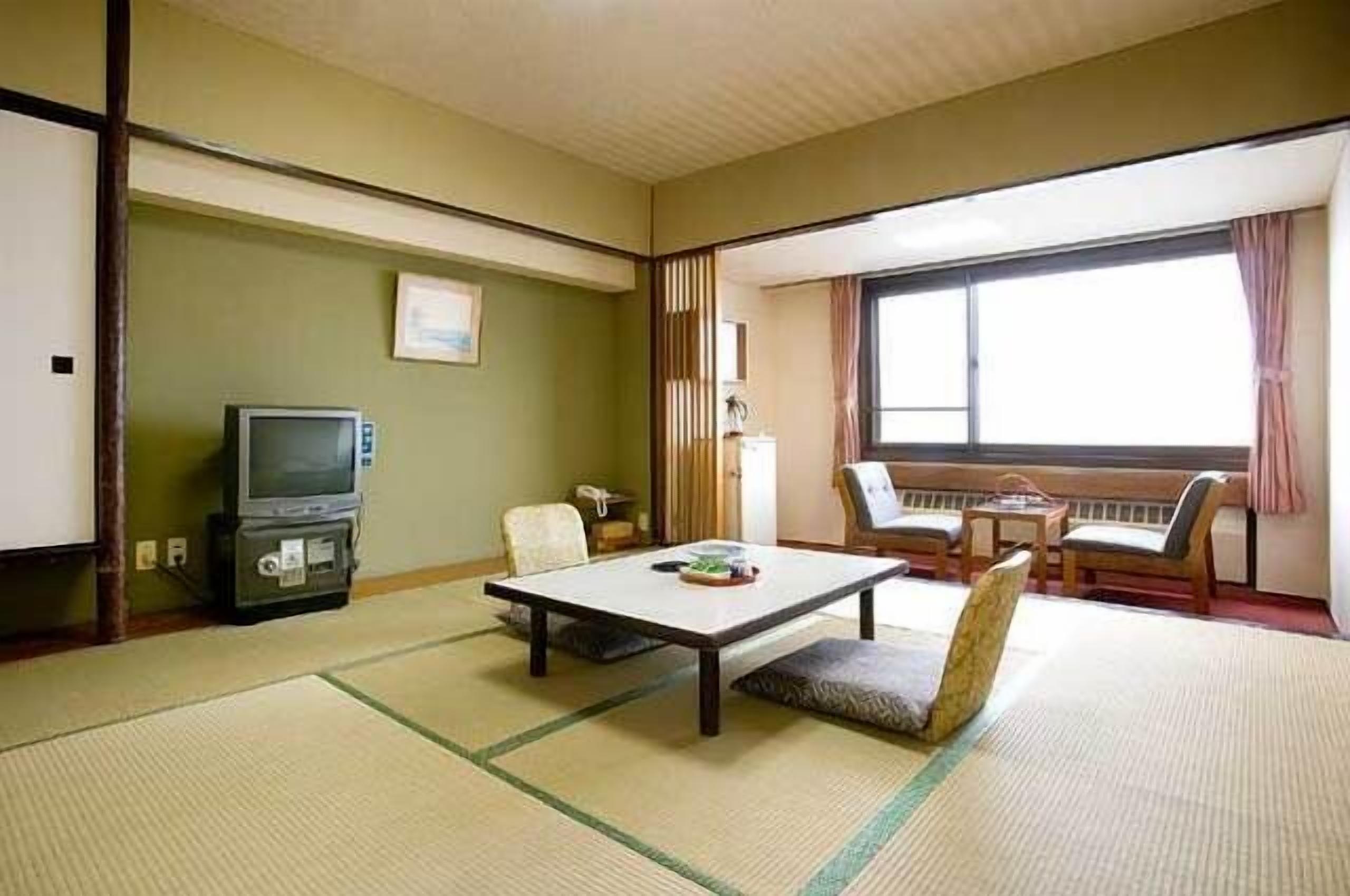 A traditional Japanese room with tatami flooring, a television, a table, and a view of the outside.