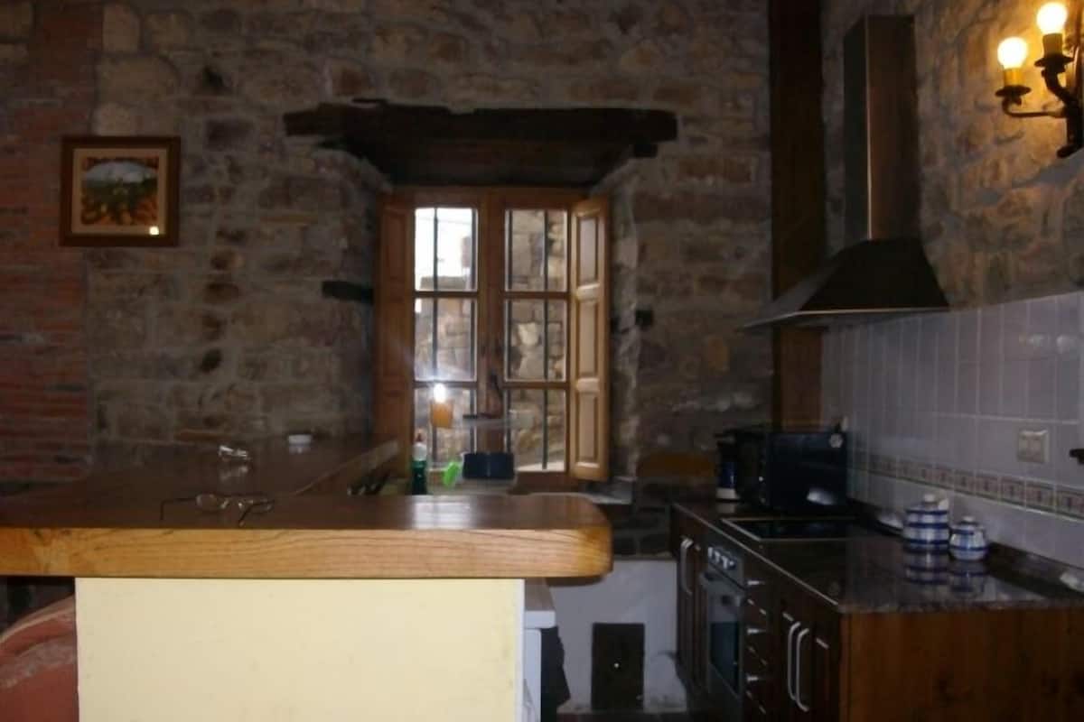 A rustic kitchen with stone walls, wooden cabinets, and a large window.