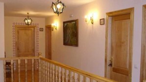 Una escalera con balaustres de madera y barandal, que conduce a un rellano con una puerta de madera y una lámpara fijada a la pared.