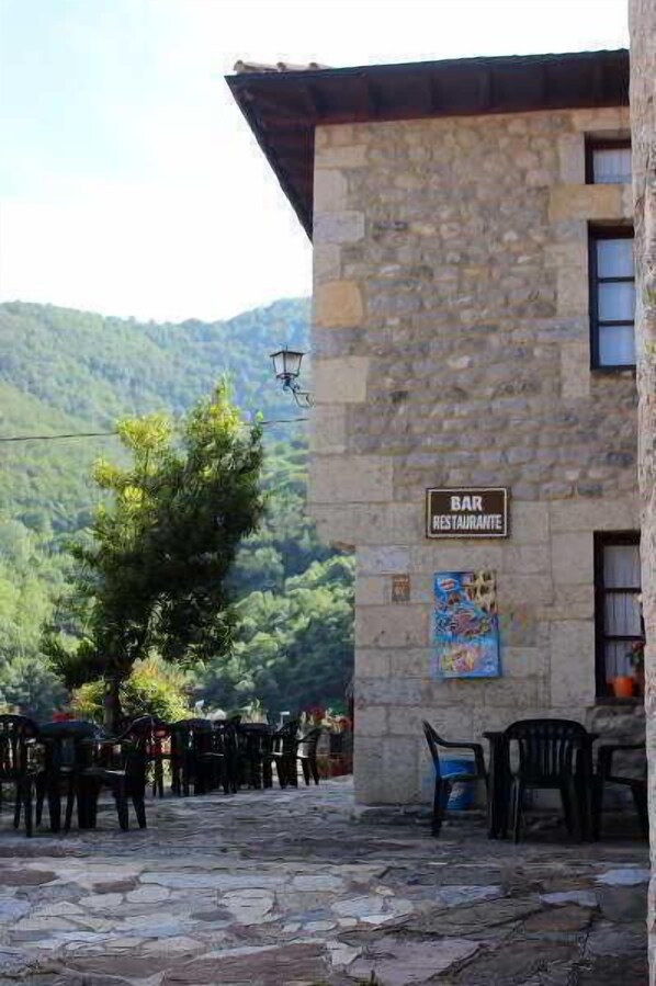 A stone building with a sign reading "BAR RESTAURANTE" and outdoor seating with plastic chairs. - Posada Sobrevilla (Camaleno)