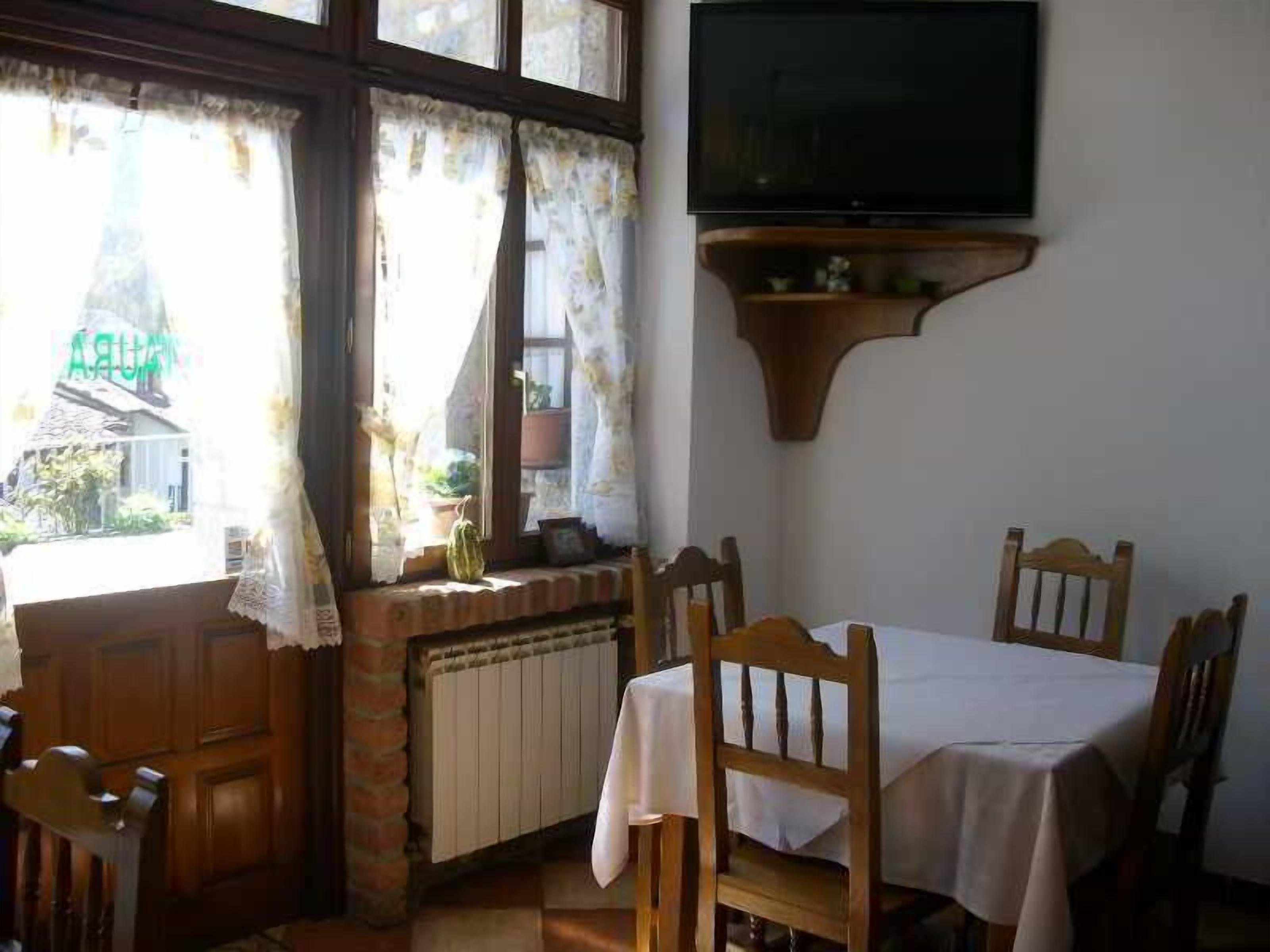 Un comedor con una mesa y sillas, un televisor montado en la pared y una ventana con cortinas.