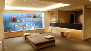 Una habitación de hotel moderna con una cama grande, un área de descanso, una recepción y estantes con diversos objetos.